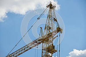 High-rise construction crane with a long arrow of yellow color against the blue sky over a new multi-storey building of concrete