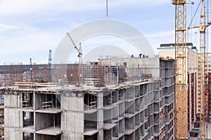 High-rise mighty hoisting crane and large building construction site with cranes with long yellow arrow against blue sky new multi