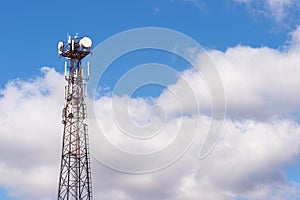 A high-rise telecommunications tower made of metal structure against a blue sky with gray clouds. Background