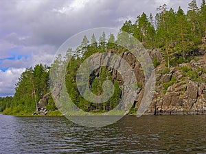 High rocky bank of the lake overgrown with pine forest photo