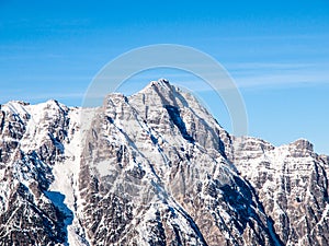 High rocky snowy peak on sunny winter day with blue sky. Alpine mountain ridge