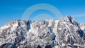 High rocky snowy peak on sunny winter day with blue sky. Alpine mountain ridge