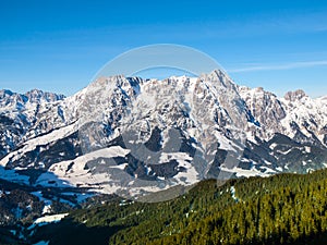 High rocky snowy peak on sunny winter day with blue sky. Alpine mountain ridge