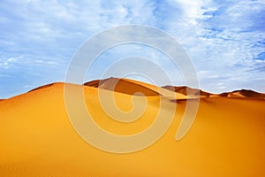 High sand dunes of the Sahara desert against a blue sky with clouds