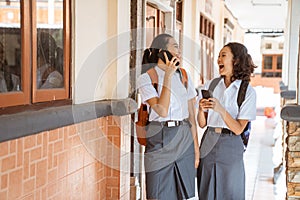 high school asian teen girls using smartphones while joking