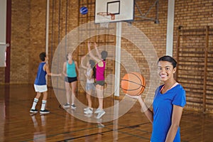 High school girl holding a basketball while team playing in background