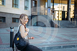 A high school student with a backpack stands on the University yard, looking at the camera and smiling, close-up.