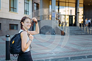 A high school student with a backpack stands on the University yard, looking at the camera and smiling, close-up