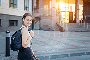 A high school student with a backpack stands on the University yard, looking at the camera and smiling, close-up