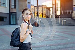 A high school student with a backpack stands on the University yard, looking at the camera and smiling, close-up