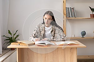 High school student taking notes from a book for study. Caucasian girl sitting at the table doing homework. Focused girl