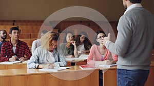 High school students are having lesson with male teacher, young people are writing and talking to tutor sitting at