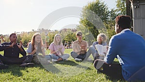 High school students sit on glass and applaud to teacher having outdoor lesson