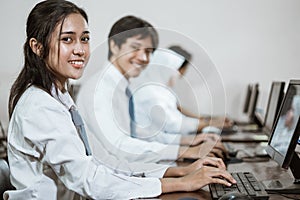 high school students smile while using a computer pc with their friends studying in a computer library room