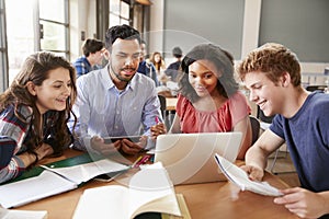 High School Students Using Laptops And Digital Tablets Working With Male Teacher At Desk