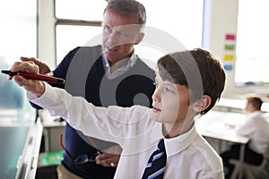 High School Teacher With Male Student Wearing Uniform Using Interactive Whiteboard During Lesson