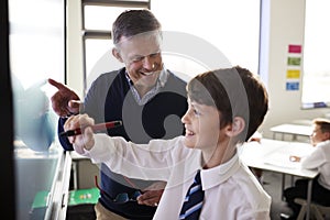 High School Teacher With Male Student Wearing Uniform Using Interactive Whiteboard During Lesson photo