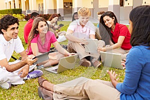 High School Teacher Sitting Outdoors With Students On Campus