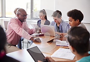 High School Teacher Talking To Pupils Using Digital Devices In Technology Class