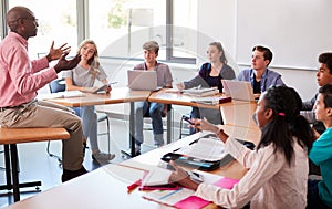 High School Teacher Talking To Pupils Using Digital Devices In Technology Class