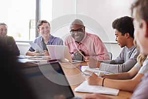 High School Teacher Talking To Pupils Using Digital Devices In Technology Class