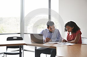 High School Tutor Giving Female Student With Laptop One To One Tuition At Desk