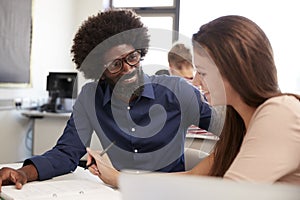 High School Tutor Giving Female Student One To One Tuition At Desk In Classroom