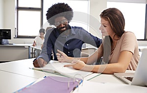 High School Tutor Giving Female Student One To One Tuition At Desk In Classroom