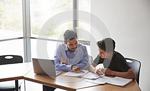 High School Tutor Giving Male Student With Laptop One To One Tuition At Desk