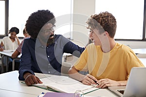 High School Tutor Giving Male Student One To One Tuition At Desk In Classroom