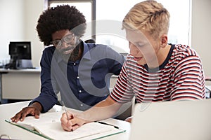 High School Tutor Giving Male Student One To One Tuition At Desk In Classroom