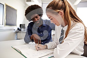 High School Tutor Giving Uniformed Female Student One To One Tuition At Desk In Classroom