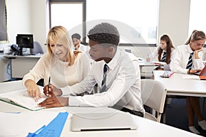 High School Tutor Giving Uniformed Male Student One To One Tuition At Desk In Classroom