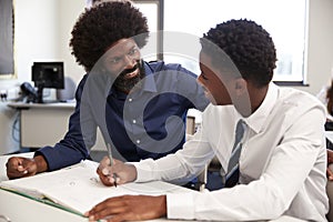 High School Tutor Giving Uniformed Male Student One To One Tuition At Desk In Classroom