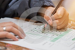 High school or university student hands taking exams, writing examination on paper answer sheet optical form of standardized test