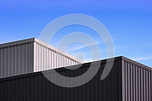 High section of 2 black and white corrugated metal Factory Buildings against blue sky background