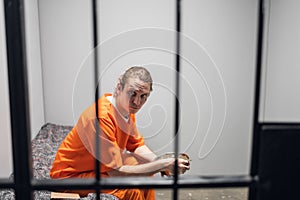 A high-security prison inmate in a red prison uniform eats from an iron bowl in his solitary cell.