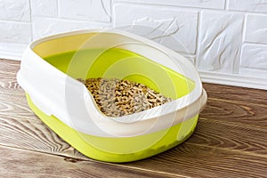 High sided cat litter tray with wooden pellets on a brown wooden floor. New green cat box near the wall. Toilet for domestic pets
