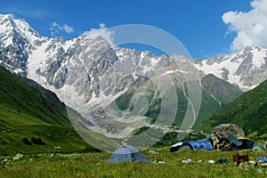 High snow mountain range above camping tents in green valley