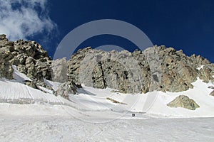 High snow and rocky mountain range, small people figures on snow