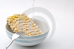 High sodium food, quick snack and meal in minutes concept with hot water pouring over instant noodles in a ceramic bowl isolated