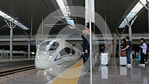 High-speed CRH bullet train approaching platform with crew driver & passengers waiting for boarding