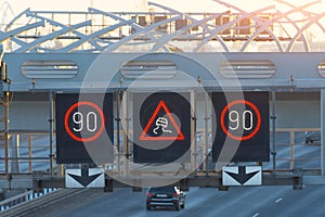 High-speed highway with traffic cars and electronic interactive speed limit signs and a slippery road warning