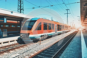 High speed orange train on the railway station at sunset