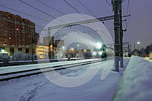 High-speed passenger electric train at night. A beam of train spotlight illuminates the falling snow