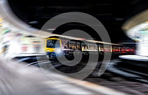 High speed passenger train rushing through train station speeding motion blur not stopping for passengers travellers and commuters