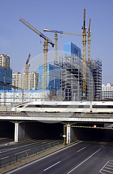 A high-speed rail train is speeding past a large infrastructure site under construction.