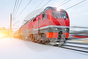 High-speed red locomotive passenger train rides at high speed in winter around the snowy landscape.