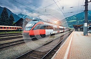 High speed train on the railway station in mountains at sunset