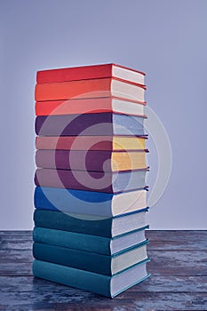 A high stack of bright thick books in multi-colored fabric covers, on a shabby wooden table.